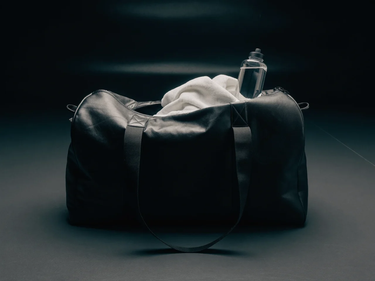Schwarze Gym-Duffelbag offen auf dem Trainingsboden, daneben Handtuch und Trinkflasche