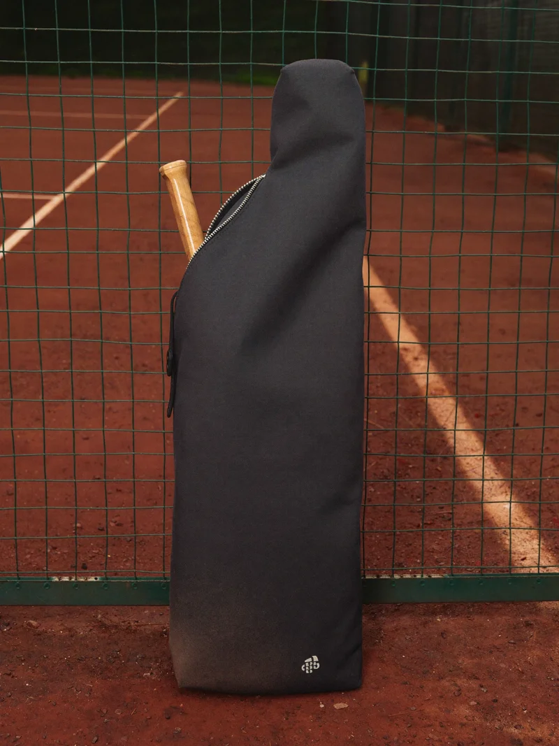 Anthrazitfarbene Tennistasche am Sandplatzzaun, Schlägergriff ragt heraus