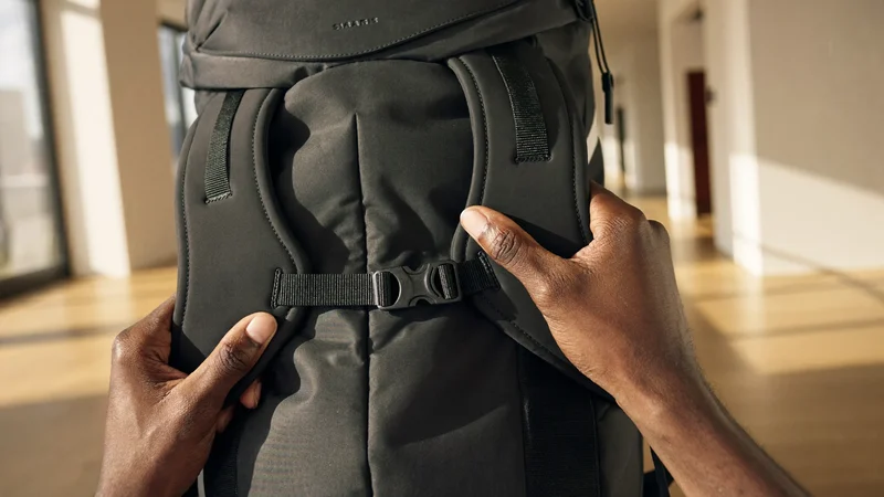 Hände stellen den Schultergurt eines Rucksacks im sonnigen Flur ein
